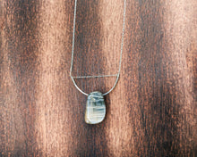 Cargar imagen en el visor de la galería, This stunning natural Black Moonstone gemstone has colors of slate grey and tan with a velvety silver flash across the surface when it is moved about in the light. This naturally-shaped Black Moonstone is set on a sterling silver half-circle, hung from a dainty sterling silver paper clip cable chain, and finished with a vintage-inspired pearl box clasp. The perfect necklace for those looking for a minimal design, but still want a unique gemstone rarely seen in most jewelry collections.
